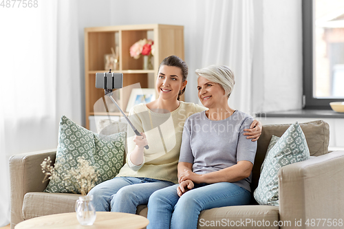 Image of senior mother with daughter taking selfie at home