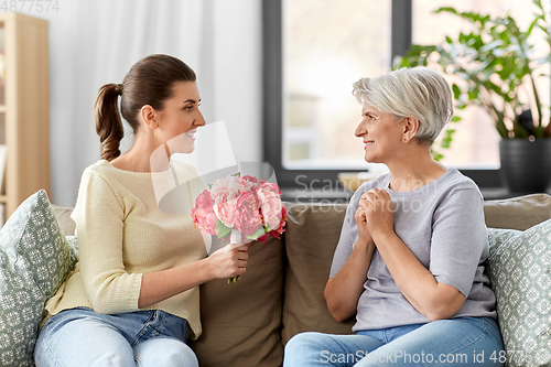 Image of adult daughter giving flowers to old mother