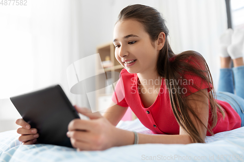Image of smiling girl with tablet pc lying on bed at home