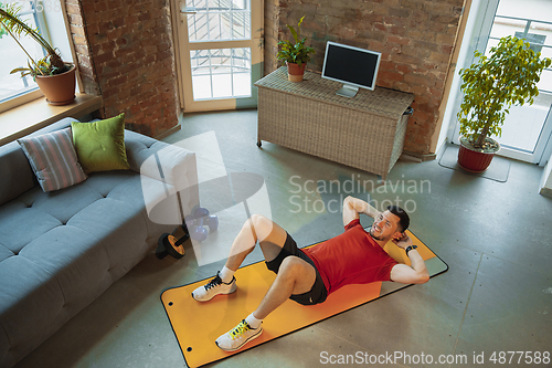 Image of Young caucasian man training at home during quarantine of coronavirus outbreak, doing exercises of fitness, aerobic. Staying sportive during insulation.