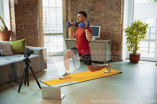 Image of Young caucasian man training at home during quarantine of coronavirus outbreak, doing exercises of fitness, aerobic. Staying sportive during insulation.