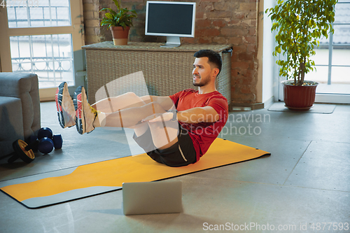 Image of Young caucasian man training at home during quarantine of coronavirus outbreak, doing exercises of fitness, aerobic. Staying sportive during insulation.