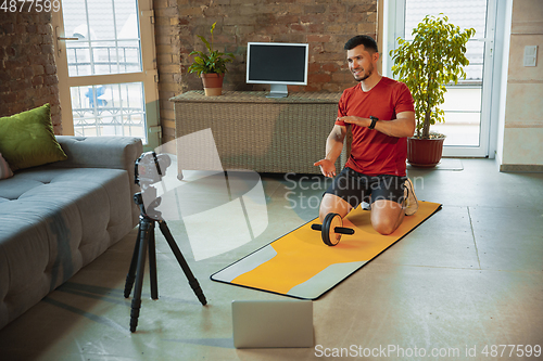 Image of Young caucasian man training at home during quarantine of coronavirus outbreak, doing exercises of fitness, aerobic. Staying sportive during insulation.