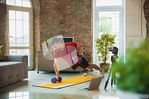 Image of Young caucasian man training at home during quarantine of coronavirus outbreak, doing exercises of fitness, aerobic. Staying sportive during insulation.