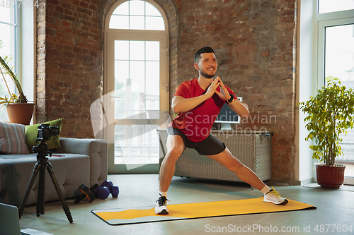 Image of Young caucasian man training at home during quarantine of coronavirus outbreak, doing exercises of fitness, aerobic. Staying sportive during insulation.