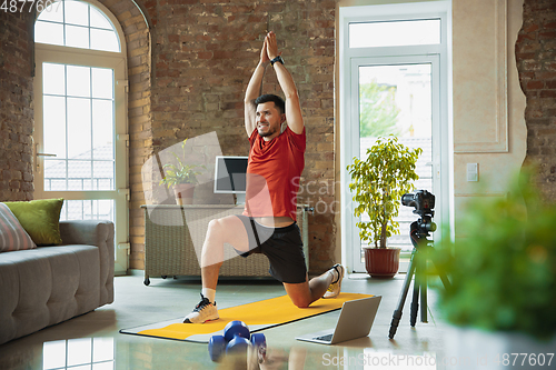 Image of Young caucasian man training at home during quarantine of coronavirus outbreak, doing exercises of fitness, aerobic. Staying sportive during insulation.