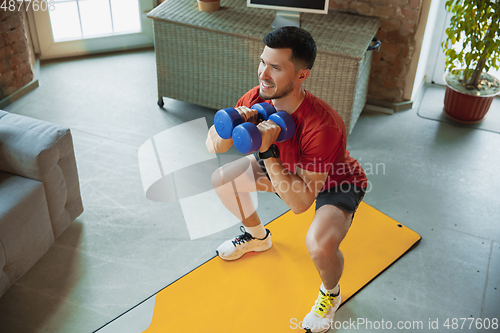 Image of Young caucasian man training at home during quarantine of coronavirus outbreak, doing exercises of fitness, aerobic. Staying sportive during insulation.