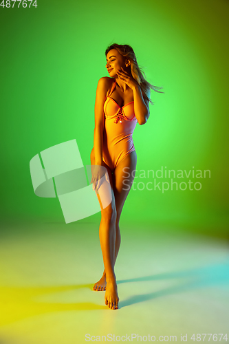 Image of Beautiful girl in fashionable swimsuit isolated on gradient studio background in neon light. Summer, resort, fashion and weekend concept