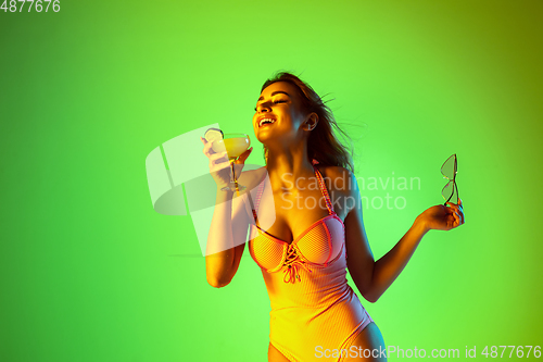 Image of Beautiful girl in fashionable swimsuit isolated on gradient studio background in neon light. Summer, resort, fashion and weekend concept