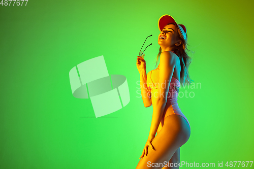 Image of Beautiful girl in fashionable swimsuit isolated on gradient studio background in neon light. Summer, resort, fashion and weekend concept