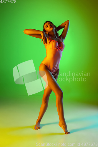 Image of Beautiful girl in fashionable swimsuit isolated on gradient studio background in neon light. Summer, resort, fashion and weekend concept