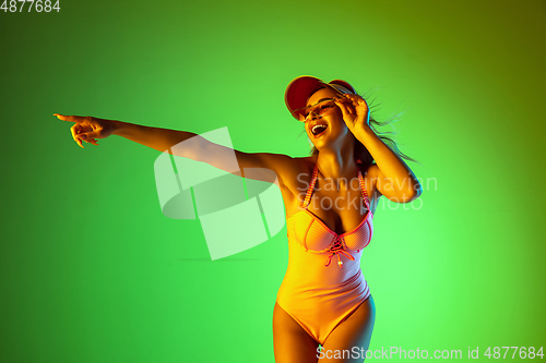 Image of Beautiful girl in fashionable swimsuit isolated on gradient studio background in neon light. Summer, resort, fashion and weekend concept