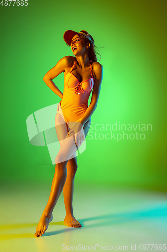 Image of Beautiful girl in fashionable swimsuit isolated on gradient studio background in neon light. Summer, resort, fashion and weekend concept