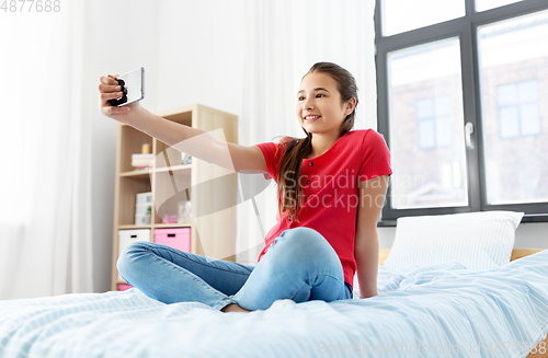 Image of happy girl with smartphone taking selfie at home