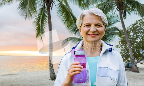 Image of sporty senior woman with bottle of water at park