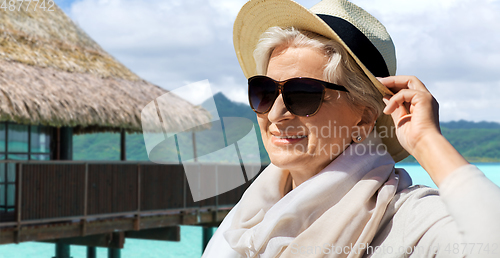 Image of happy senior woman in sunglasses and hat on beach