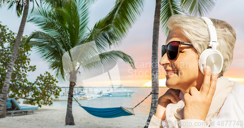 Image of old woman in headphones listens to music on beach