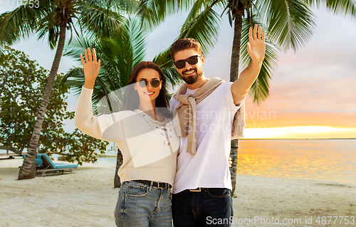 Image of happy couple waving hands on beach