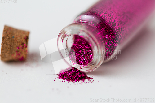 Image of pink glitters poured from small glass bottle