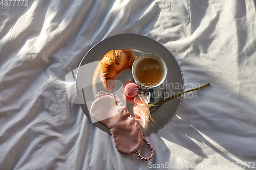 Image of croissant, coffee and eye sleeping mask in bed