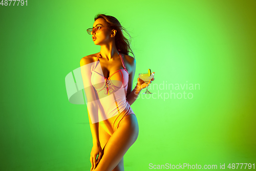 Image of Beautiful girl in fashionable swimsuit isolated on gradient studio background in neon light. Summer, resort, fashion and weekend concept