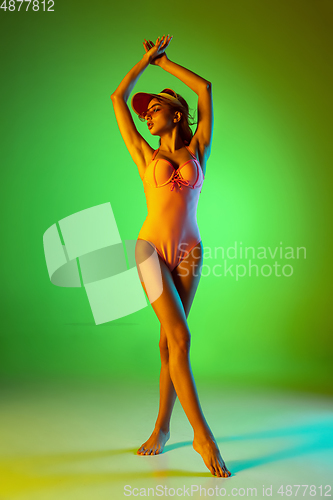 Image of Beautiful girl in fashionable swimsuit isolated on gradient studio background in neon light. Summer, resort, fashion and weekend concept