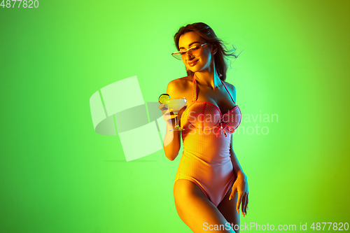 Image of Beautiful girl in fashionable swimsuit isolated on gradient studio background in neon light. Summer, resort, fashion and weekend concept