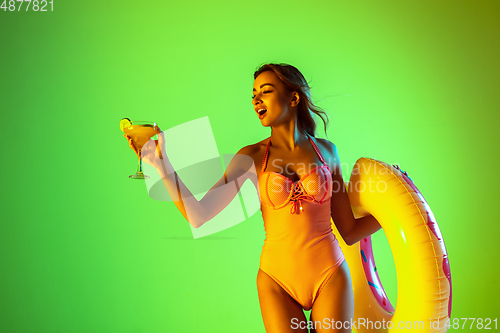 Image of Beautiful girl in fashionable swimsuit isolated on gradient studio background in neon light. Summer, resort, fashion and weekend concept