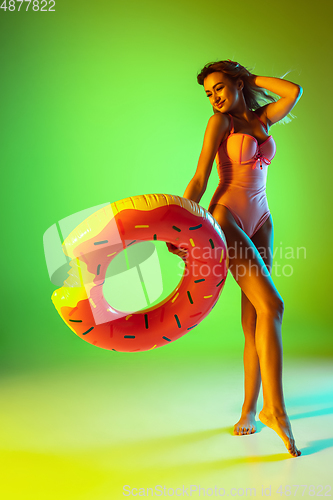 Image of Beautiful girl in fashionable swimsuit isolated on gradient studio background in neon light. Summer, resort, fashion and weekend concept