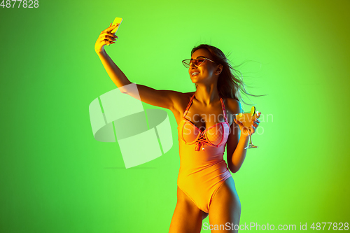 Image of Beautiful girl in fashionable swimsuit isolated on gradient studio background in neon light. Summer, resort, fashion and weekend concept
