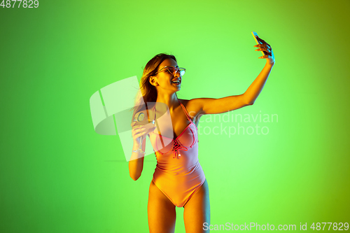 Image of Beautiful girl in fashionable swimsuit isolated on gradient studio background in neon light. Summer, resort, fashion and weekend concept