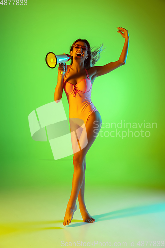 Image of Beautiful girl in fashionable swimsuit isolated on gradient studio background in neon light. Summer, resort, fashion and weekend concept