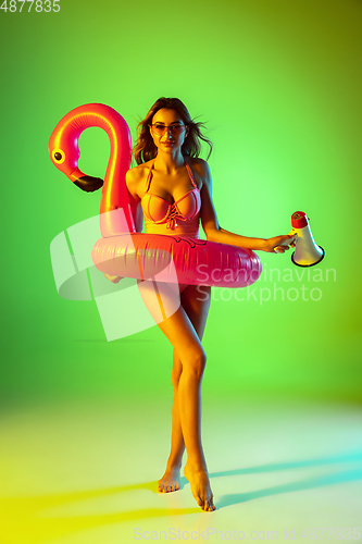 Image of Beautiful girl in fashionable swimsuit isolated on gradient studio background in neon light. Summer, resort, fashion and weekend concept