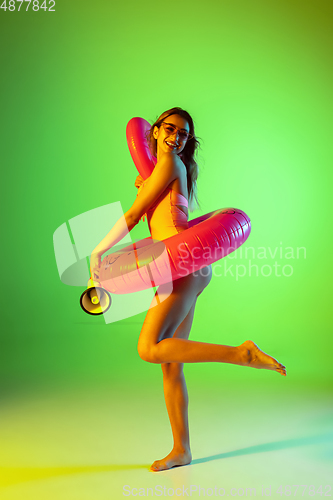 Image of Beautiful girl in fashionable swimsuit isolated on gradient studio background in neon light. Summer, resort, fashion and weekend concept