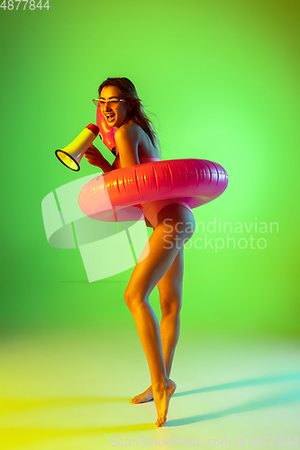 Image of Beautiful girl in fashionable swimsuit isolated on gradient studio background in neon light. Summer, resort, fashion and weekend concept