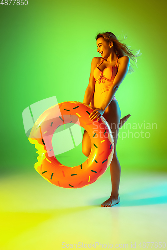 Image of Beautiful girl in fashionable swimsuit isolated on gradient studio background in neon light. Summer, resort, fashion and weekend concept