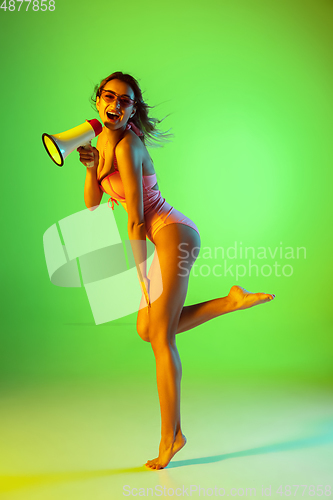 Image of Beautiful girl in fashionable swimsuit isolated on gradient studio background in neon light. Summer, resort, fashion and weekend concept