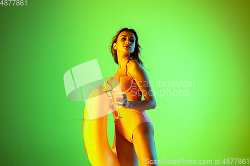 Image of Beautiful girl in fashionable swimsuit isolated on gradient studio background in neon light. Summer, resort, fashion and weekend concept