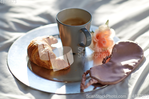 Image of croissant, coffee and eye sleeping mask in bed