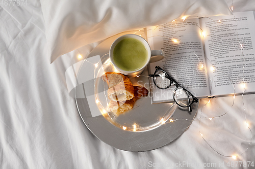 Image of croissants, matcha tea, book and glasses in bed