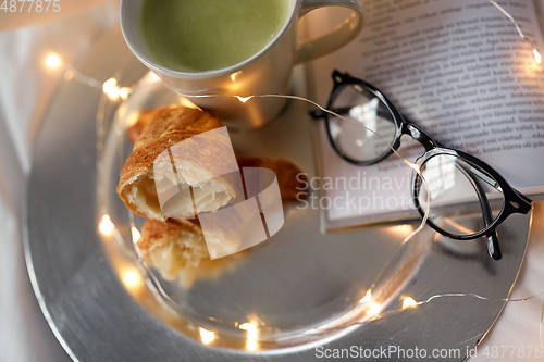 Image of croissants, matcha tea, book and glasses in bed