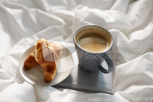 Image of croissants, cup of coffee and book in bed at home