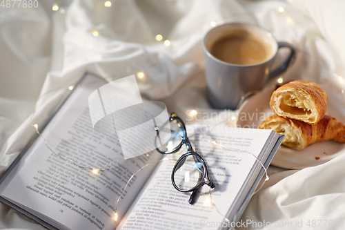 Image of croissants, cup of coffee, book and glasses in bed