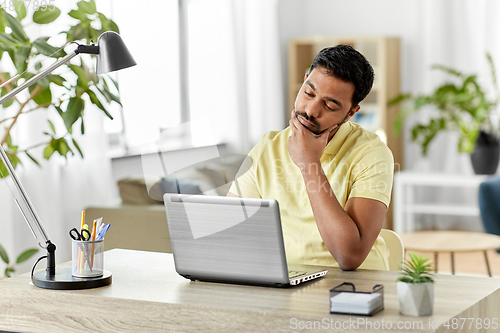 Image of indian man with laptop thinking at home office