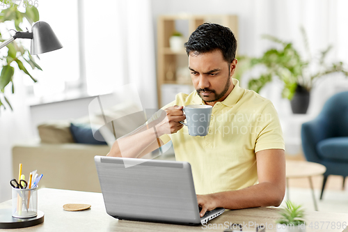 Image of man with laptop drinking coffee at home office