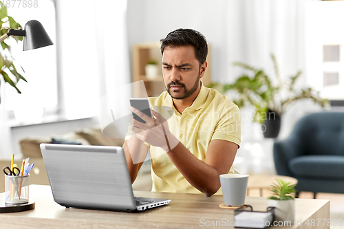 Image of happy indian man with smartphone at home office