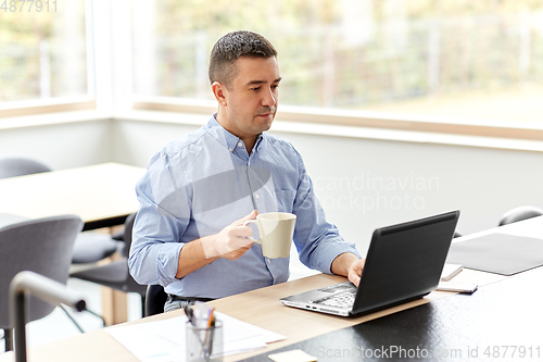 Image of man with laptop drinking coffee at home office
