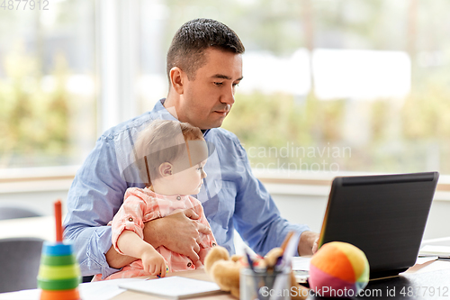 Image of father with baby working on laptop at home office