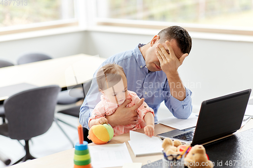 Image of father with baby working on laptop at home office