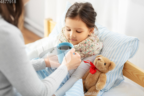 Image of mother giving hot tea to sick little daughter